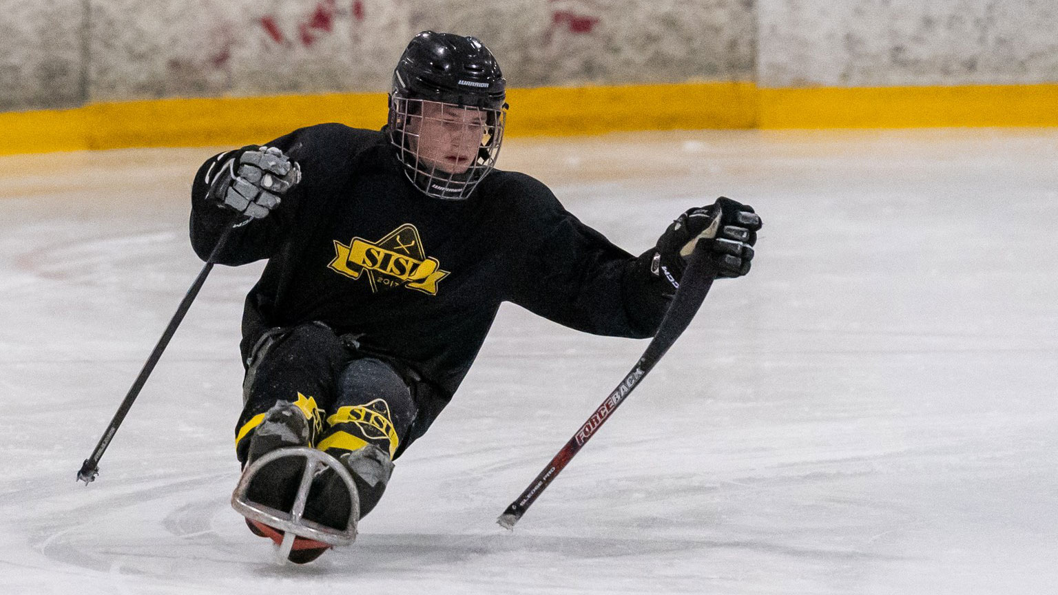 Iiro luistelemassa jäällä kelkan kanssa SISU Paraicehockeyn pelivarustus päällä.